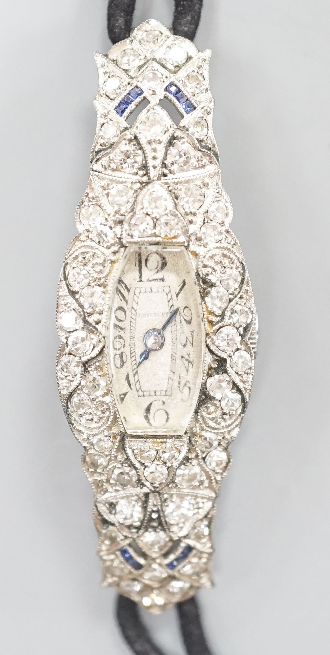 A lady's mid 20th century engraved white metal, diamond and sapphire set cocktail watch, case diameter 17mm, gross weight 18.3 grams, on a later? twin strand fabric strap.